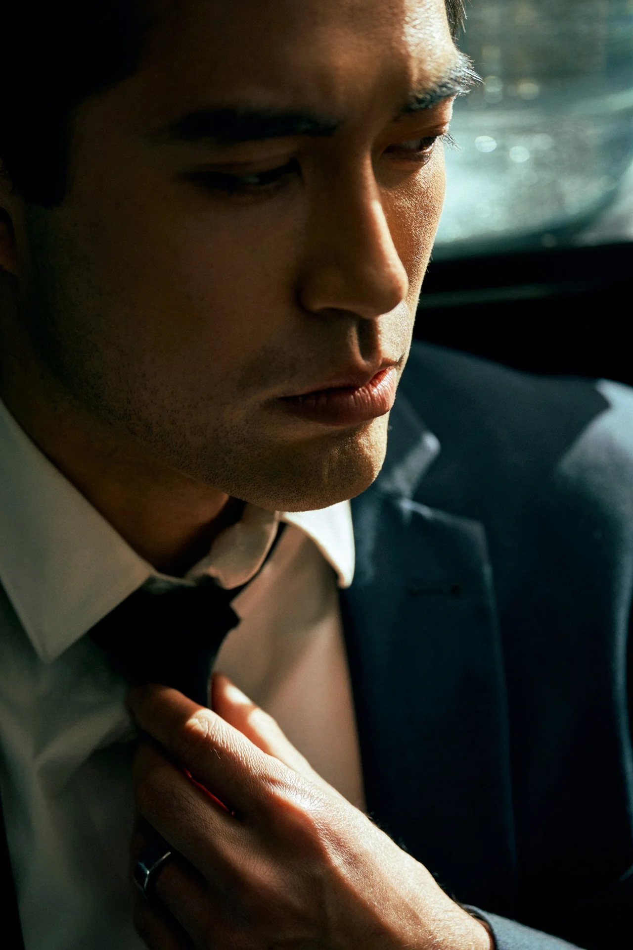 A close editorial portrait of Damien Sato adjusting his tie