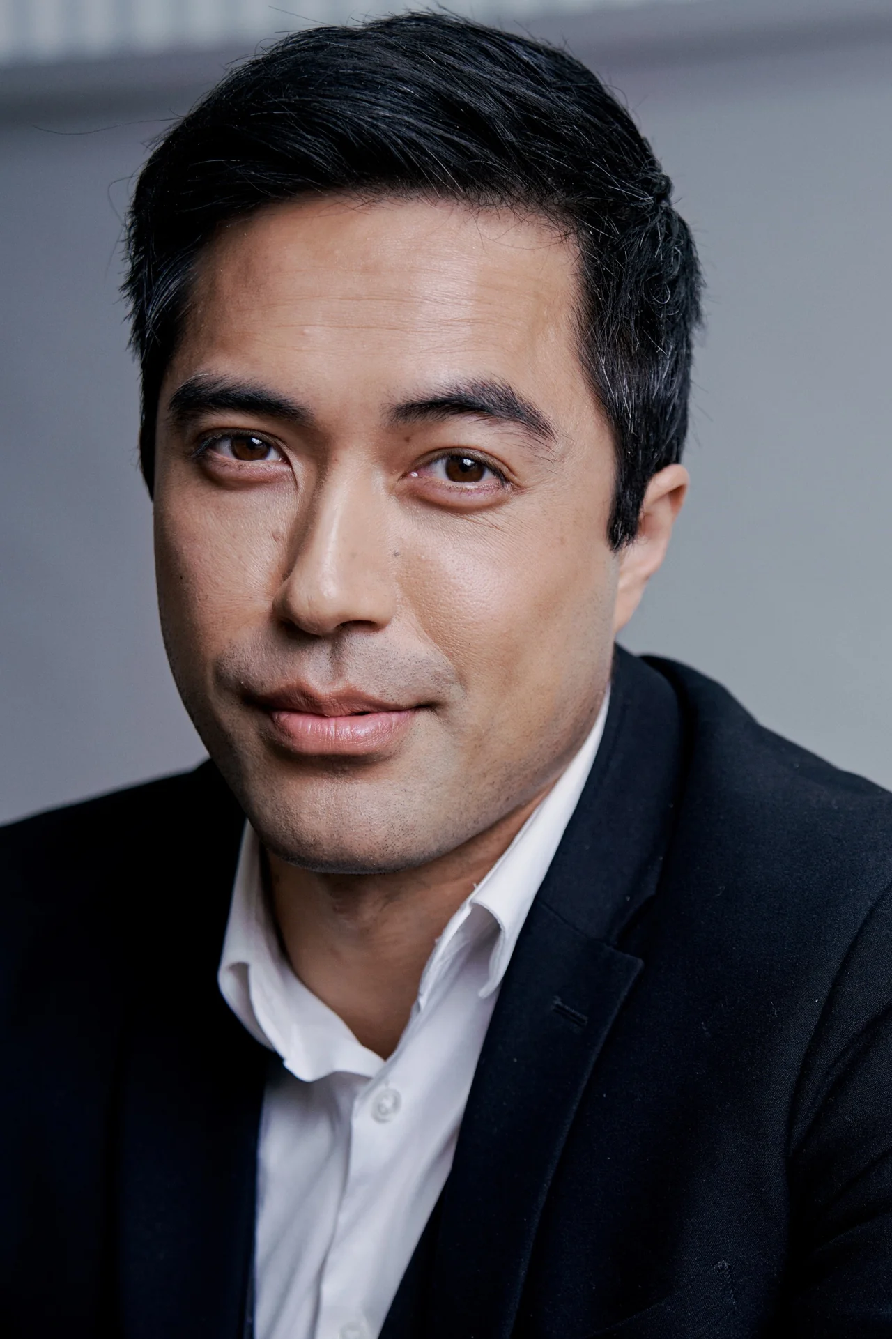 Damien Sato in a dark jacket and open white shirt