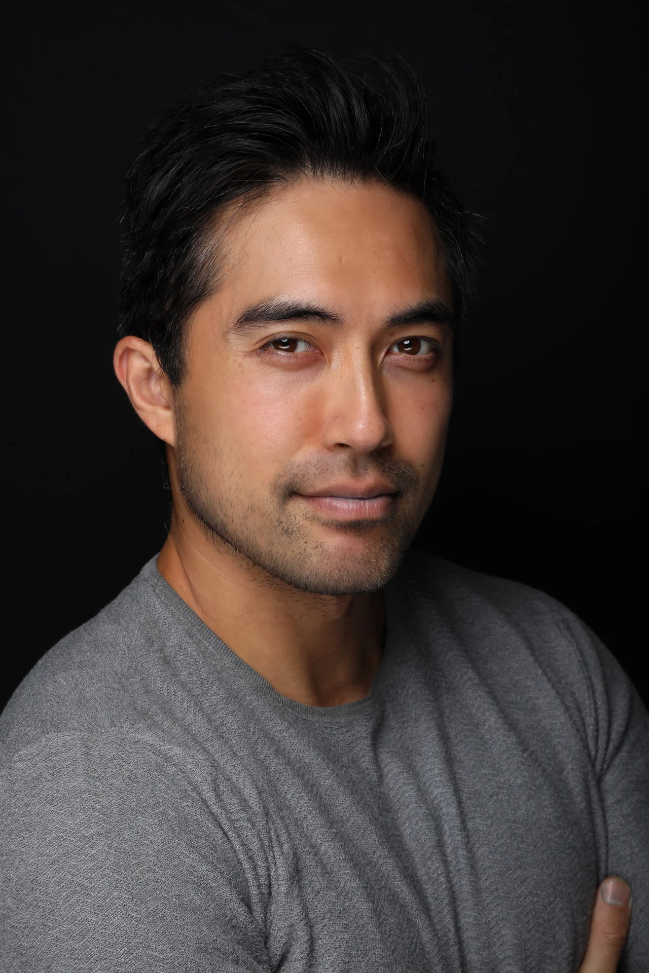 Damien Sato in a grey shirt, photographed against a dark background